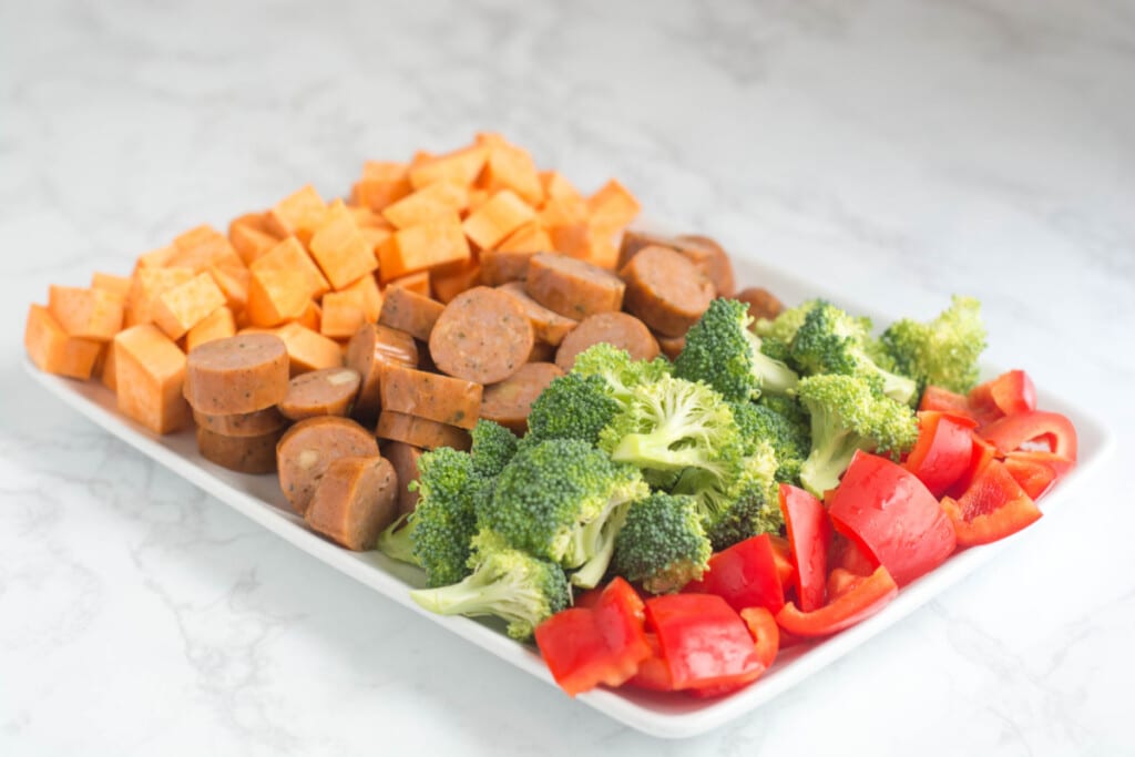 A white plate with cut-up sweet potatoes, sausage, broccoli, and red pepper.