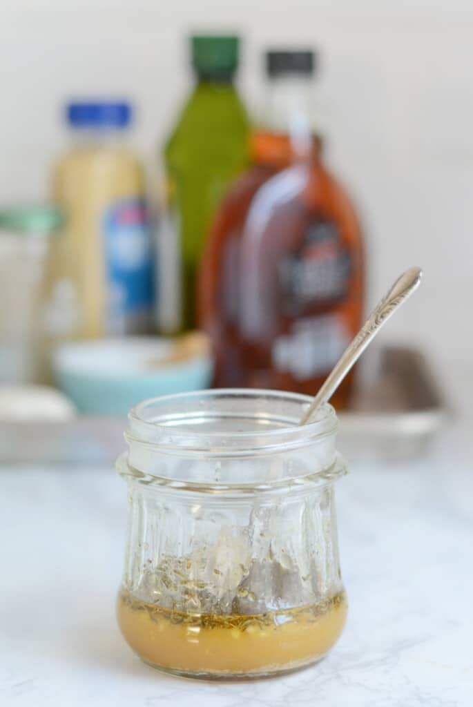 A small jar of sauce sits on. acounter with a silver spoon inside.